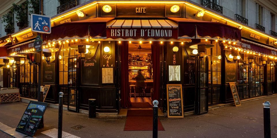 Bistrot d’Edmond at night — corner of rue Monsigny, illuminated awnings and string lights, the rue Monsigny street sign on the left