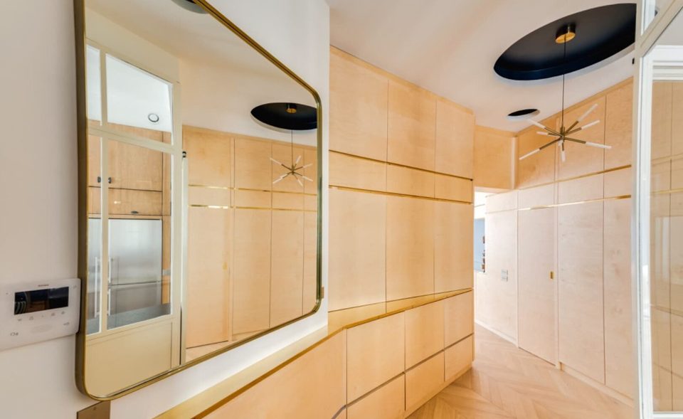 Entry corridor with brass-framed mirror reflecting the kitchen verrière and maple millwork