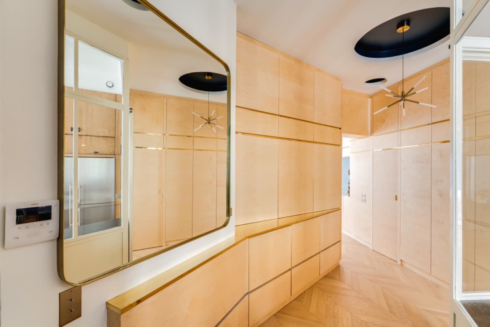 Entry corridor with brass-framed mirror reflecting the kitchen verrière and maple millwork