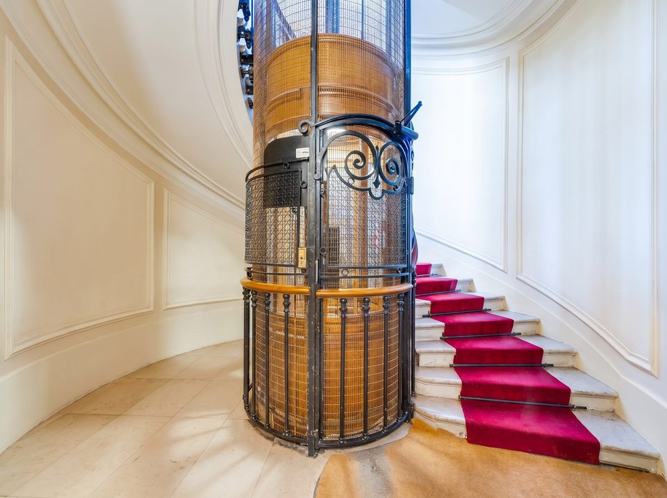 Building lobby — period iron-cage elevator and marble staircase with red carpet