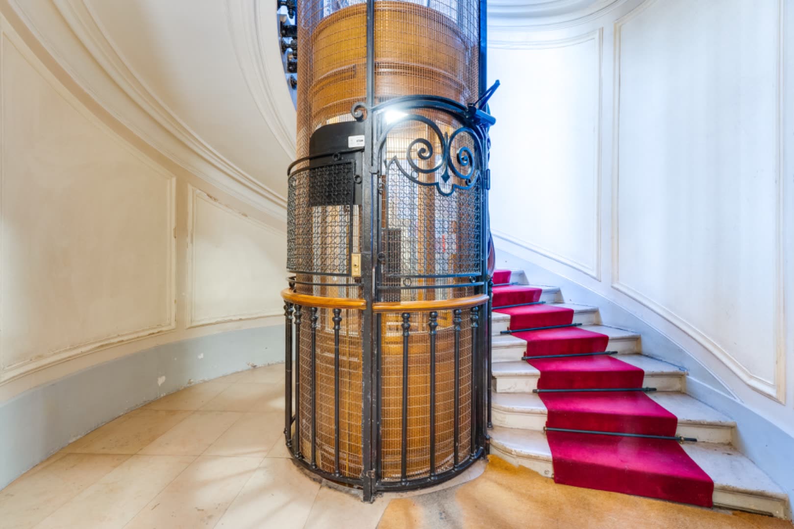 Building lobby — period iron-cage elevator and marble staircase with red carpet