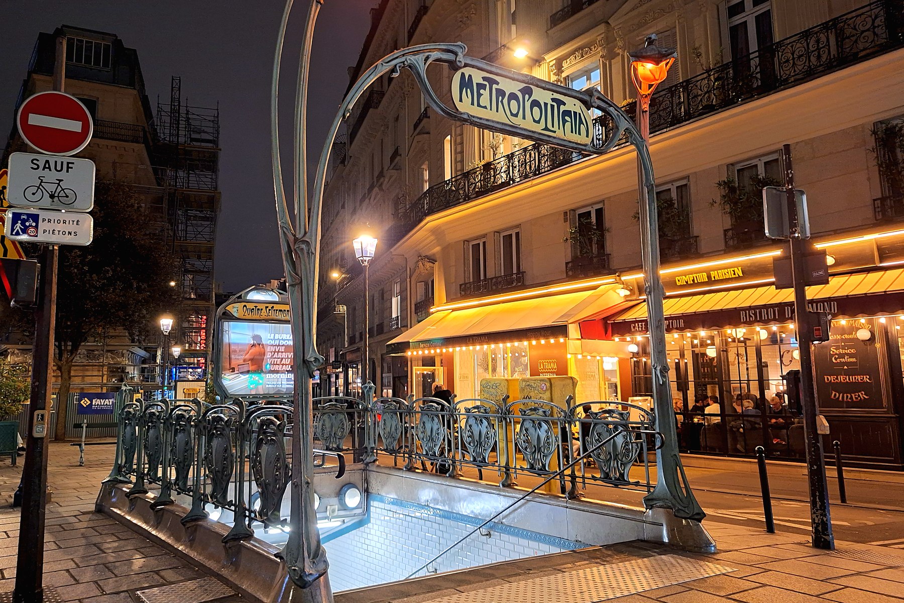 Métro Quatre-Septembre at night — Art Nouveau Guimard entrance on rue du 4 Septembre, with Comptoir Parisien and Bistrot d’Edmond illuminated in warm amber light, a few steps from 19 rue Monsigny, Paris 2e