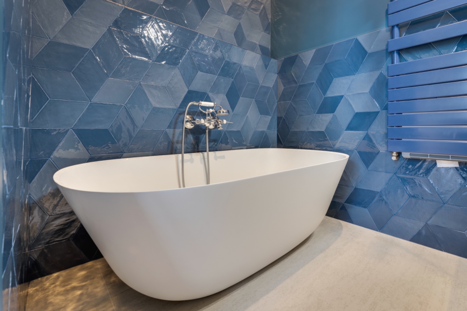 Freestanding white tub set against deep blue diamond-cut tiles